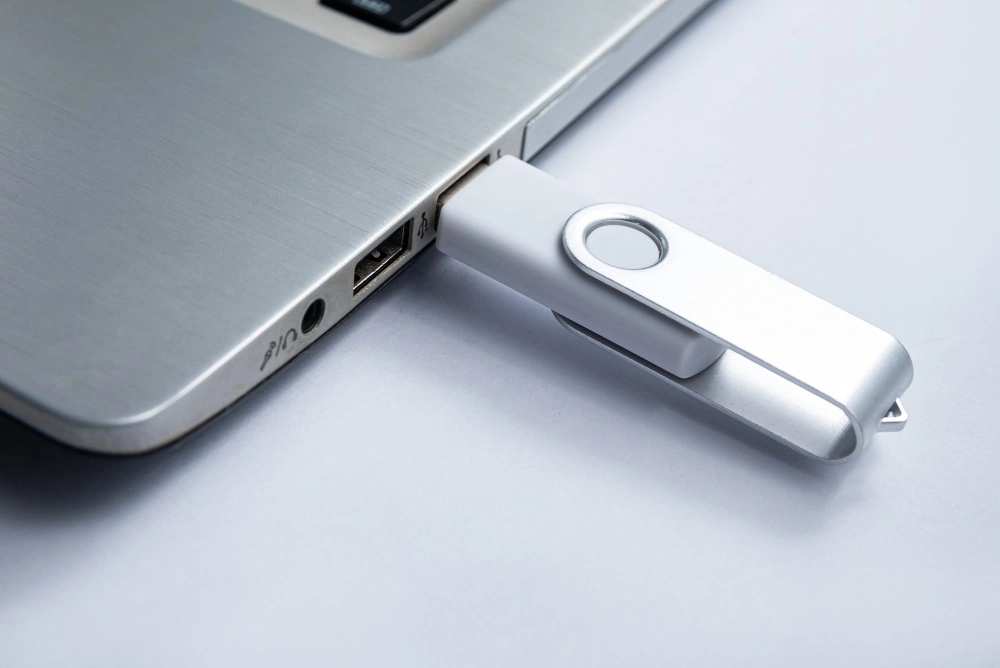 Branded silver flash drive beside a laptop, an example of custom USB printing Dubai companies order for corporate gifts