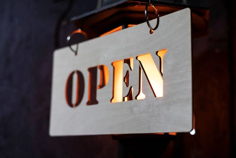 Laser cut wooden OPEN sign glowing above a shopfront entrance at night